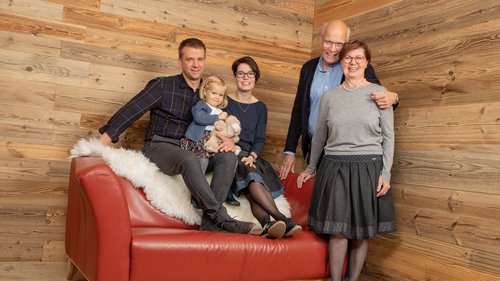 Wählt hier eure Ferienwohnung im Allgäu! Fünfköpfige Familie auf rotem Sofa in Holzzimmer