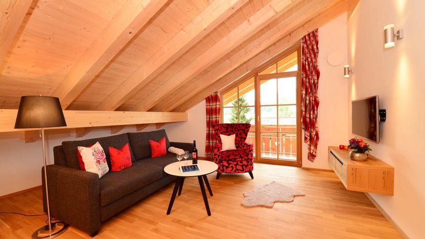 Hotel und Ferienwohnung im Allgäu, Oberstdorf Gemütliches Wohnzimmer mit Holzbalkendecke, Sofa, Sessel und Balkonblick