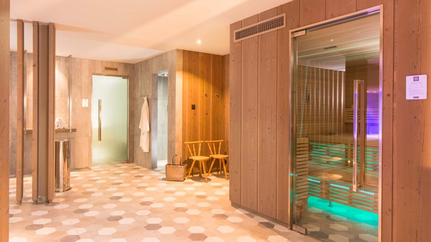 Hotel und Ferienwohnung im Allgäu, Oberstdorf Moderner Saunabereich mit Holzvertäfelung, Glastür und zwei Holzstühlen