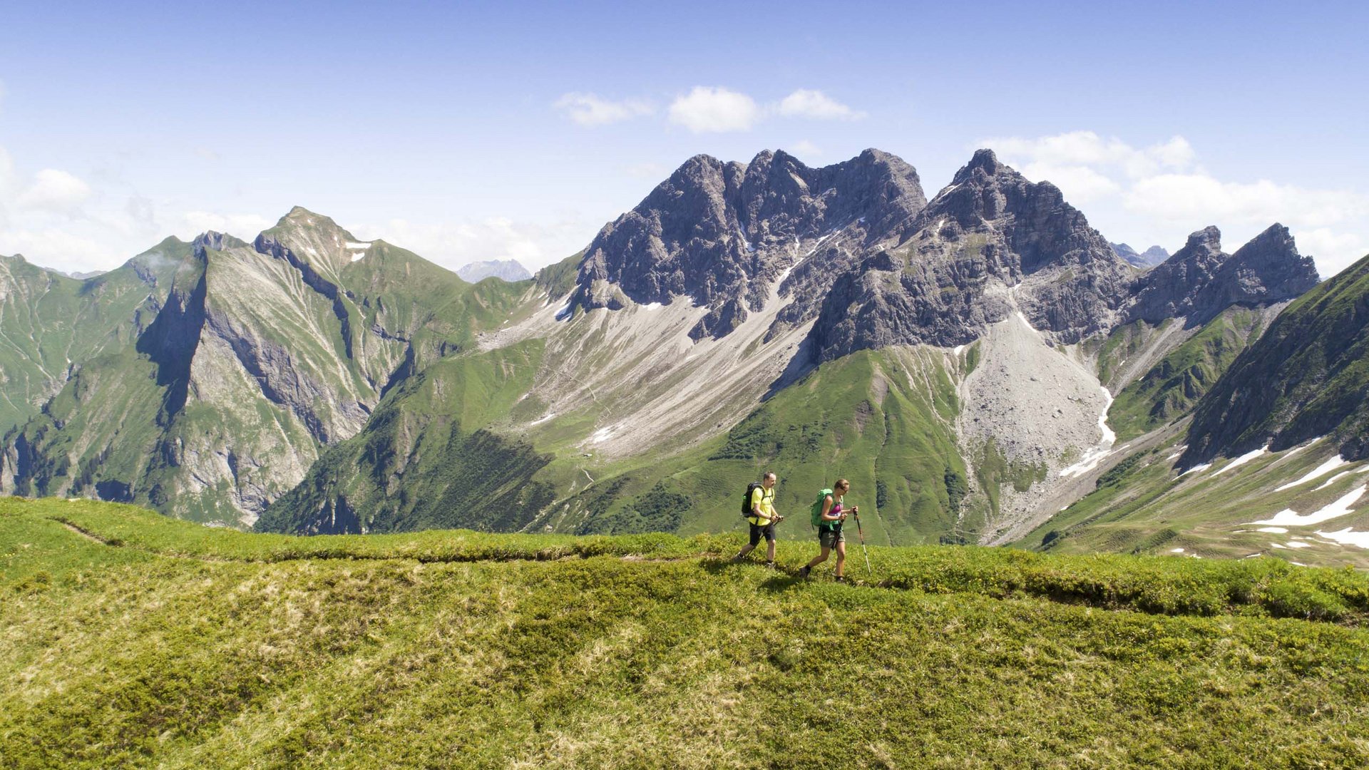 Plan your holiday in Oberstdorf Two hikers on green mountain meadow with alpine peaks and blue sky background