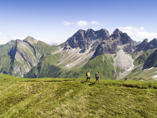 Hahnenköpfle: holiday apartment, lodge & hotel in Oberstdorf Two hikers on green mountain meadow with alpine peaks and blue sky background