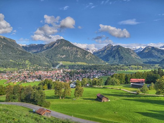 Hahnenköpfle: holiday apartment, lodge & hotel in Oberstdorf View of a town in a valley with mountains and green fields under clear sky