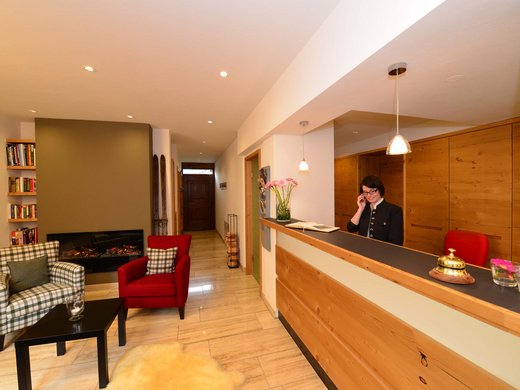 Hotel oder Ferienwohnung in Oberstdorf? Beides! Empfangsbereich mit Rezeptionistin in einem gemütlichen Hotel mit Kamin