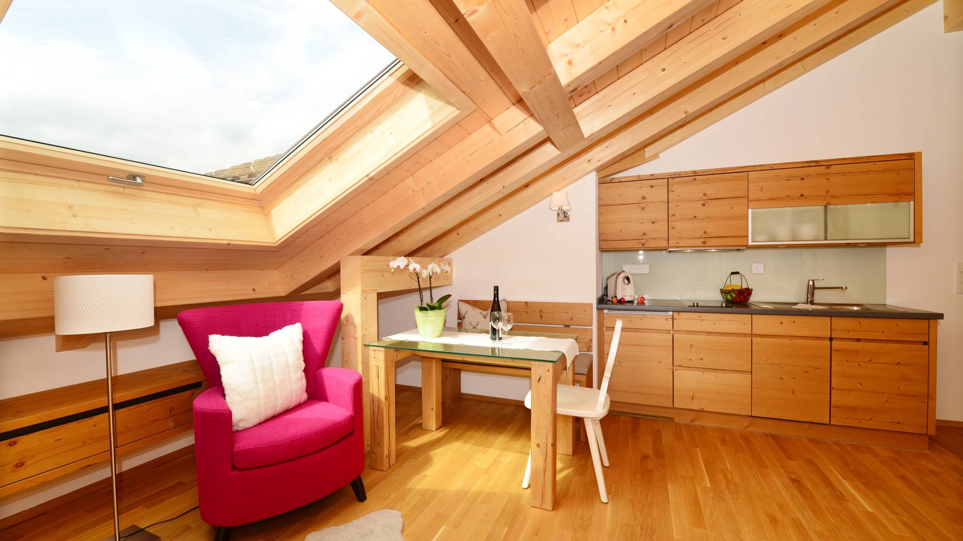 Hotel und Ferienwohnung im Allgäu, Oberstdorf Gemütliche Dachgeschossküche mit Holzmöbeln und pinkem Sessel unter Dachfenster