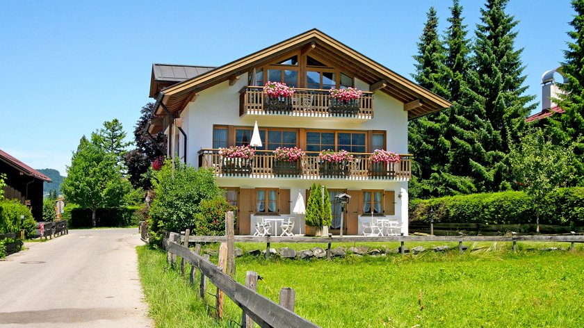 Hotel und Ferienwohnung im Allgäu, Oberstdorf Haus mit Balkonen und Blumen an einer Landstraße im Grünen